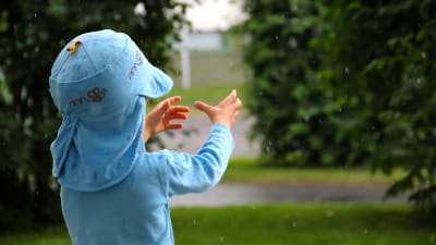 Ett litet barn fösöker fånga regnet med händerna.