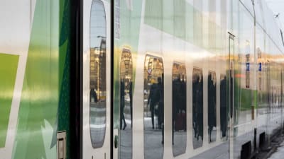 Fjärrtåg vid en perrong, närbild av vagnens fönster som reflekterar passagerare.