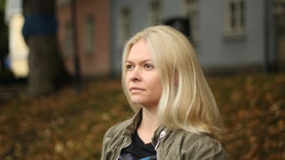 En blond kvinna står vid åstranden i Åbo och tittar bort från kameran.