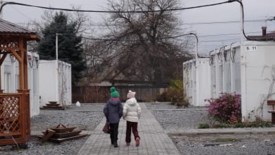 Två skolflickor går på en gång mellan tillfälliga bostadsbaracker
