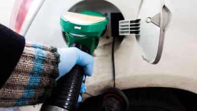 En kvinna fyller på bensin i bilens tank. 
