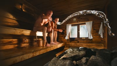 En man och en kvinna sitter i en bastu. Mannen kastar löyly.