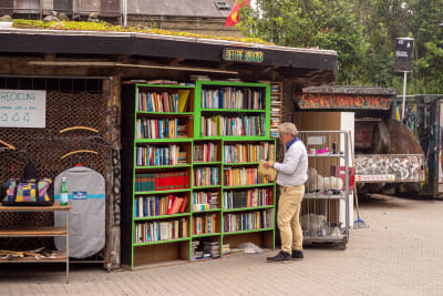 En man står framför ett utebibliotek och bläddrar i en bok.