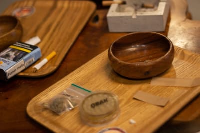 Brickor med cannabis, tobak, rullpapper och en grinder på ett bord.