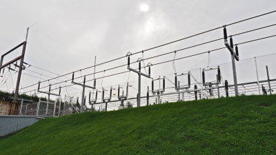 Elledningar som löper från en eldistributionscentral avtecknar sig mot himlen ovanför en gräsklädd slänt.