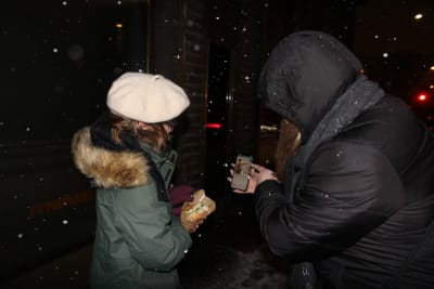 ett barn och en vuxen står ute i snöyran och tittar på en telefonskärm.