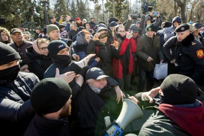 Maskerade poliser griper en man under en demonstration.