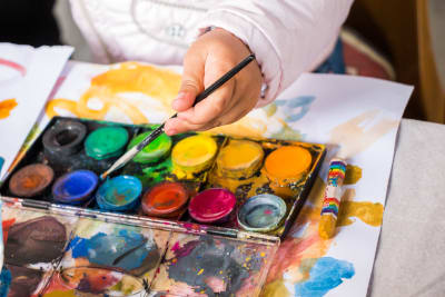 Olika färger av vattenfärg och handen av ett barn som håller i en pensel.
