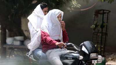 Två män åker motorcykel. De har skyddat sina ansikten med vita dukar på grund av den extrema hettan i New Delhi.