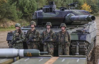 Fyra soldater i uniform och hjälm står framför en Leopard 2-stridsvagn. 
