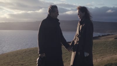 Reynolds Woodcock (Daniel Day-Lewis) och Alma (Vicky Krieps) står och håller varandra i handen vid en hög sluttning ner mot havet.
