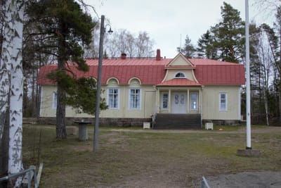Stort gräddgult trähus från 1920-talet med rött mansardtak.