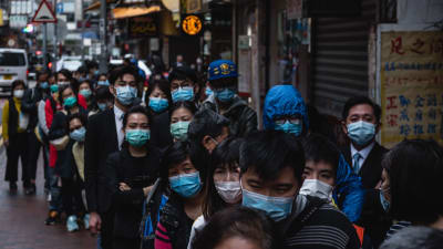 En lång kö med människor med ansiktsmask på en gata i en stad. 