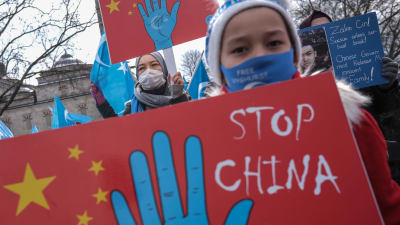 En kvinna med blått munskydd håller upp ett plakat med texten "Stop China".