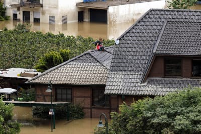 Kvinna sitter på taket till ett hus. Vattennivån omkring husen är hög.