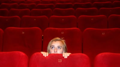 En kvinna i en tom biografsal kryper ihop bakom stolen och tittat försiktigt fram.