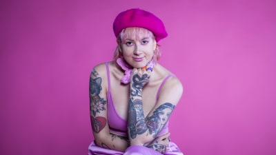Ronja Stanley sitter på en stol framför en rosa vägg och ser rakt in i kameran och ler.