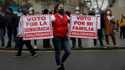 En peruansk demonstrant håller upp plakat där det står en uppmaning om att stöda demokrati och inte kommunism.