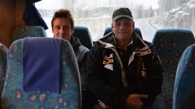 Två män på bakbänken i en buss. 