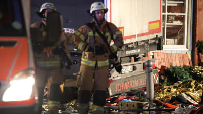 Två brandmän står vid lastbilen som körde in i en folksamling på en julmarknad i Berlin.