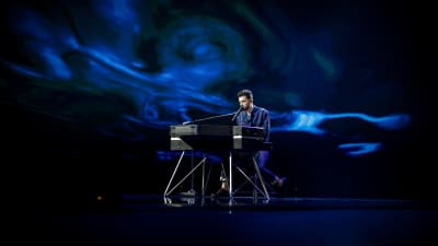 duncan laurence sjunger sittandes vid ett elpiano och har ett blått skimmer runtom sig