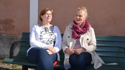 Eija och Pilvi på en bänk i solskenet.