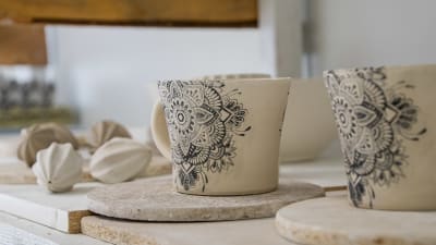 En keramikmugg med mönster står och torkar på en hylla, bland med andra keramikföremål.