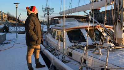 Bild av en man i vinterkläder som står och tittr på en segelbåt. 