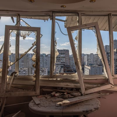 Pommituksessa vahingoittuneen asuinkerrostalon rikkoutuneiden ikkounoiden läpi näkymä kerrostaloalueelle.