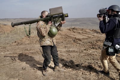Sotilas kantaa asetta ja kuvaaja kuvaa kameralla sotilasta.