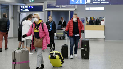 Resenärer som drar på resväskor och bär andningsskydd.