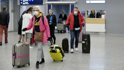 Flygpassagerare med ansiktsskydd drar sitt bagage på flygplatsen.