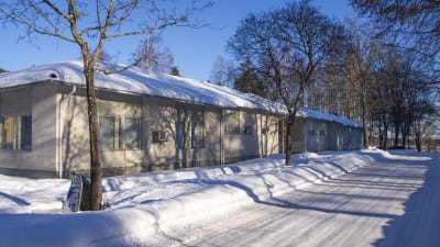 En rappad byggnad i en våning, täckt i snö. Till höger i bild syns en plogad väg.