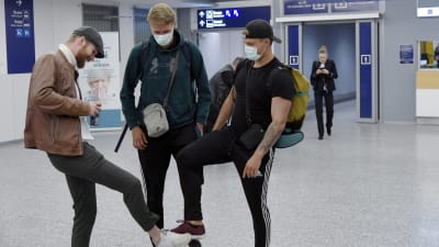 Tre unga män hälsar genom att "skaka fot" med varandra på Helsingfors-Vanda flygplats.