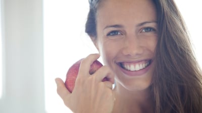 Leende kvinna håller ett äpple.