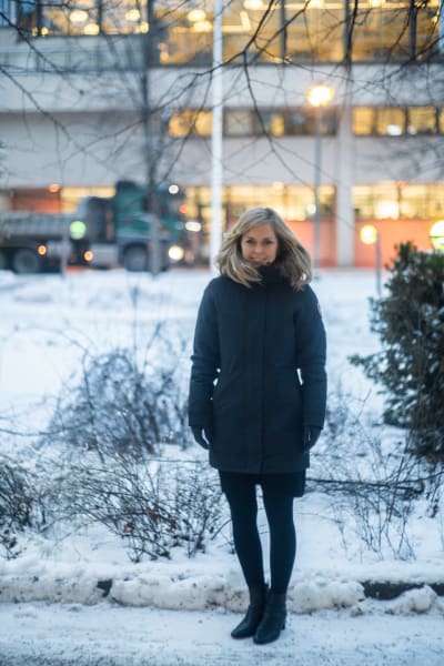 En kvinna står i en snöig stadsmiljö. Hon ser glad ut. 