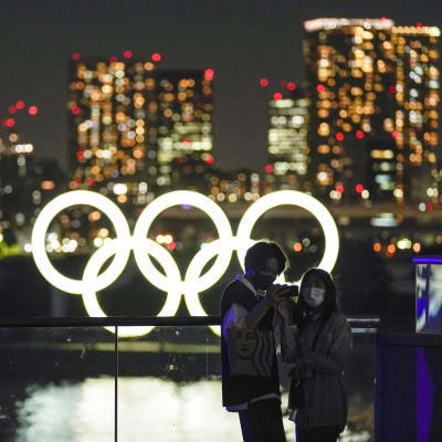 Nuoret valokuvaavat itseään iltavalossa olympiarenkaiden edessä Tokiossa.