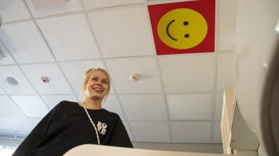 En kvinna står vid ett skötbord och i taket syns en glad smiley.