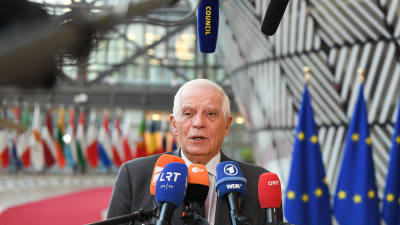 Josep Borrell med en rad mikrofoner framför sig och EU-flaggor samt många olika länders flaggor bakom sig.