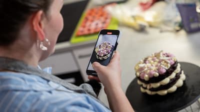 En kvinna står och filmar en dekorativ tårta med sin mobiltelefon.