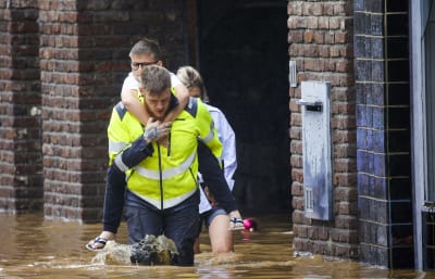 En man bär en pojke på sin rygg genom översvämningar i Belgien. 
