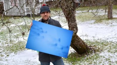 Fotograf står ute med sin bild i famnen.