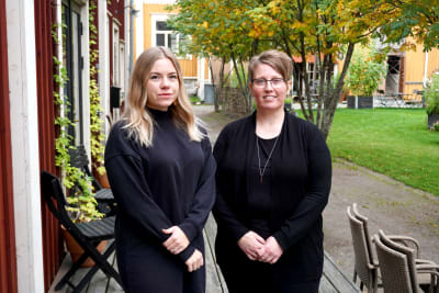 Två svartklädda kvinnor står på en veranda.