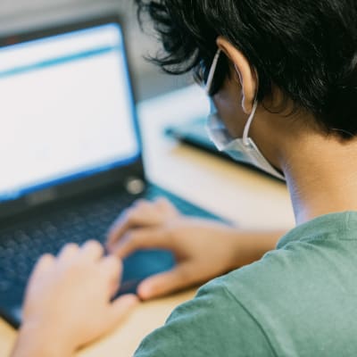 Oppilas käyttää tietokonetta kasvomaski päällään.