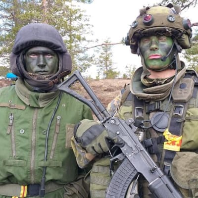 Kaksi vihreän kasvovärin avulla naamioitunutta sotilasta seisoo rinnkkain. Toisella rinnalla rynnäkkökivääri. 