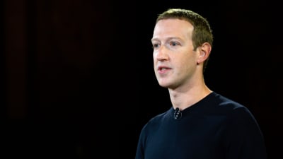 Facebooks vd Mark Zuckenberg mot en svart bakgrund. Han talar och har en svart liten knappmikrofon fast i sin mörkblå tröja.