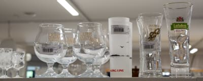 Glas med prislappar står på rad på en hylla i en loppis.