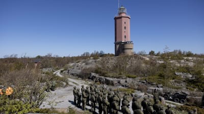 Sotilasrivistön edessä Merivoimien komentaja Jori Harju käsi lipassa. Taustalla kallioinen saari ja punainen Russarön majakka. 