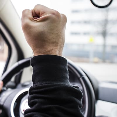 Henkilöauton kuljettaja näyttää nyrkkiä tiellä kulkevalle.