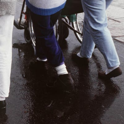 Hoitajat työntävät liikuntavammaisia pyörätuoleissa.